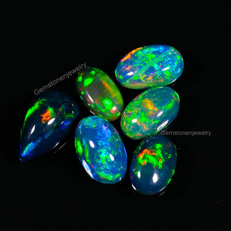 May include: Six oval-shaped black opals with green, blue, and orange iridescent flashes. The opals are arranged in a cluster on a black background.