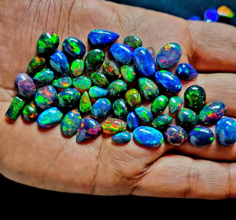 May include: A collection of loose, iridescent black opals in various shapes and sizes. The opals have a rainbow of colors, including green, blue, and red.