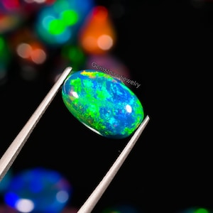 May include: A green, blue, and black oval opal gemstone with a bright iridescent sheen. The opal is held in tweezers against a black background.