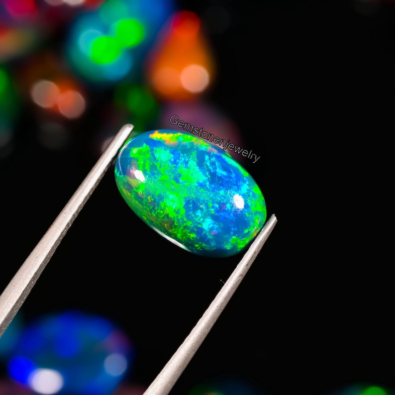 May include: A green, blue, and black oval opal gemstone with a bright iridescent sheen. The opal is held in tweezers against a black background.