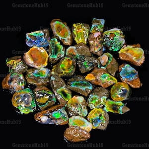 May include: A collection of rough opal stones with iridescent colors, including green, blue, orange, and yellow. The stones are on a black background.