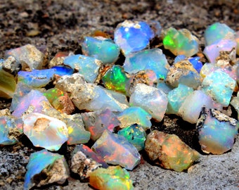 May include: A collection of rough opal gemstones in various shades of blue, green, and white. The opals are scattered on a rough, grey surface.