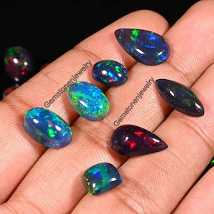 May include: Assortment of black opal gemstones in various shapes and sizes, including teardrop, oval, and rectangular. The opals display a range of iridescent colors, including green, blue, and red.