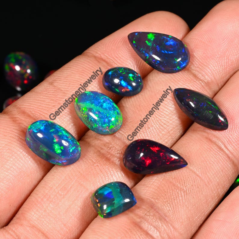 May include: Assortment of black opal gemstones in various shapes and sizes, including teardrop, oval, and rectangular. The opals display a range of iridescent colors, including green, blue, and red.