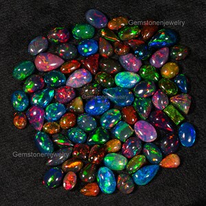 May include: A collection of approximately 50 loose, natural black opals in various shapes and sizes. The opals are iridescent with flashes of green, blue, red, and purple.