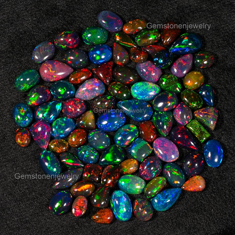 May include: A collection of approximately 50 loose, natural black opals in various shapes and sizes. The opals are iridescent with flashes of green, blue, red, and purple.