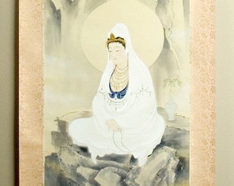 May include: A traditional Japanese scroll painting featuring a seated figure in white robes against a backdrop of a waterfall and mountains. The artwork has a gold border and is suspended by decorative ribbons.