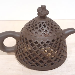 Op de afbeelding: Een bruine theepot van keramiek met een traliewerkontwerp en een deksel met een knop bovenop.