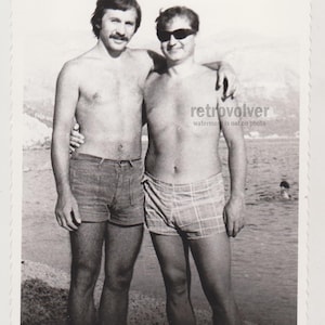 Dois jovens bonitos e carinhosos sem camisa abraçam-se com calções volumosos gays int beefcake nus troncos praia rapazes instantâneo original encontrado foto
