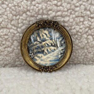 May include: A small, framed painting of a winter scene with trees and a path. The frame is gold and has a decorative design.