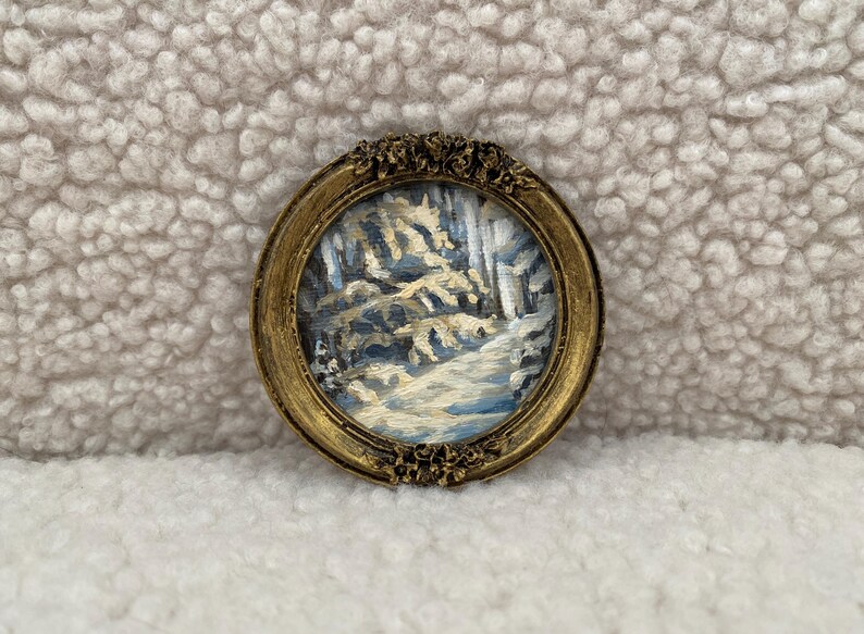 May include: A small, framed painting of a winter scene with trees and a path. The frame is gold and has a decorative design.