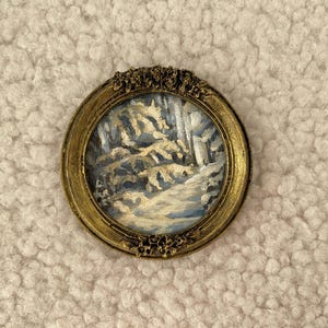 May include: A small, framed painting of a winter scene with white and blue trees and a snowy path. The frame is gold with a decorative design.