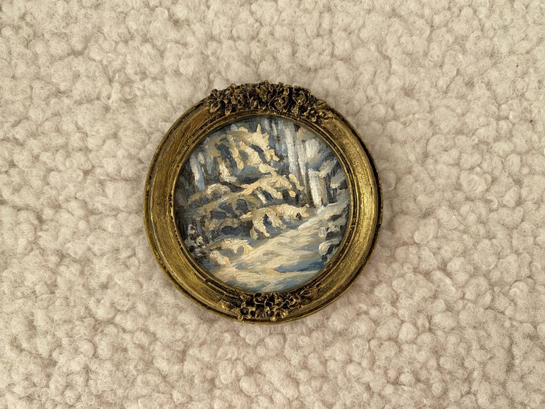 May include: A small, framed painting of a winter scene with white and blue trees and a snowy path. The frame is gold with a decorative design.