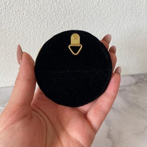 May include: A black round wall hanging with a gold metal hook on the back.
