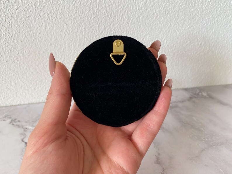 May include: A black round wall hanging with a gold metal hook on the back.