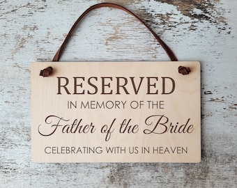 Może przedstawiać: Drewniany znak z brązowymi skórzanymi paskami wiszącymi u góry. Znak głosi "RESERVED IN MEMORY OF THE Father of the Bride CELEBRATING WITH US IN HEAVEN".