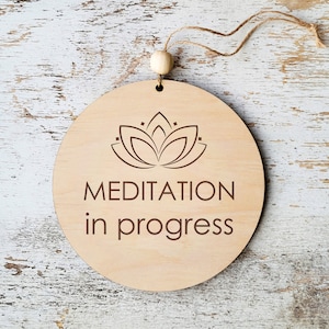 Könnte beinhalten: Ein rundes Holzschild mit einem braunen Lotusblüten-Design und dem Text "MEDITATION in progress".