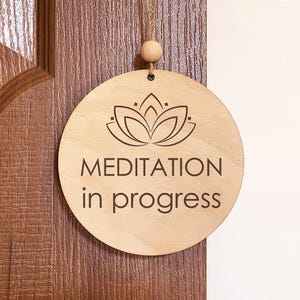 Könnte beinhalten: Ein Holzschild mit einem Lotusblumen-Design und dem Text "Meditation im Gange".