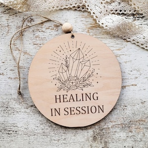 Könnte beinhalten: Ein rundes Holzschild mit einem Kristalldesign und dem Text "HEALING IN SESSION".