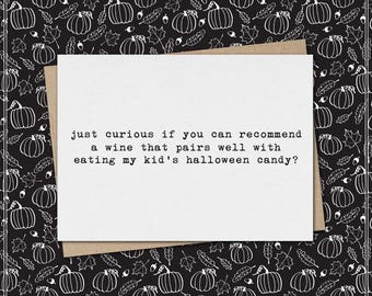 May include: A white rectangular greeting card with black typewriter-style text that reads: just curious if you can recommend a wine that pairs well with eating my kid's halloween candy? The card rests on a black background with white pumpkins.