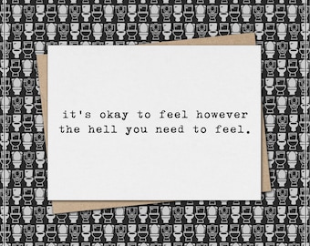 May include: A greeting card with the message "it's okay to feel however the hell you need to feel." The card is white with a brown envelope, set against a black and white toilet pattern background.