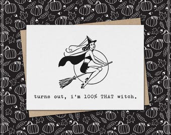May include: A white greeting card featuring a black ink illustration of a witch flying on a broomstick in front of a full moon. Below the illustration, the text reads, turns out, i'm 100% THAT witch. The card rests on a brown envelope.