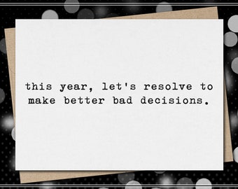May include: A white greeting card with the text "this year, let's resolve to make better bad decisions." The card is on a brown envelope, set against a black and white polka dot background.
