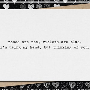 May include: A white greeting card with the text "roses are red, violets are blue. I'm using my hand, but thinking of you." The card is on a brown envelope, with a black and white heart-patterned border.