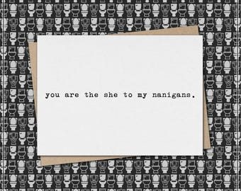 Puede incluir: Tarjeta de felicitación blanca con el texto "you are the she to my nanigans" en fuente negra. La tarjeta está sobre un sobre marrón, sobre un fondo de patrón de inodoros en blanco y negro. Diseño humorístico y único.