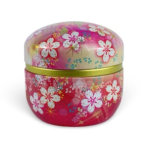 May include: A round, lidded container with a floral design. The container is primarily red with white and pink cherry blossom flowers. The lid and base are separated by a gold band. The background is white.