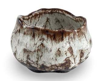 May include: A white and brown ceramic bowl with an irregular, wavy rim. The bowl has a mottled glaze with brown and white streaks.