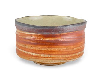 May include: A handmade ceramic bowl with a wide, open design. The bowl features horizontal bands of orange, brown, and tan hues. The rim is dark brown, and the interior is a light beige color. The bowl is likely used for serving or display.