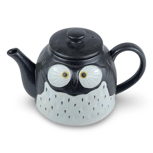 May include: Black ceramic teapot with a white owl design. The owl has large, round eyes with yellow pupils. The teapot has a spout and a handle.