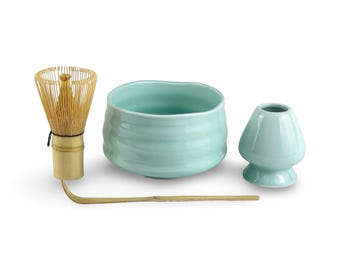 May include: A matcha tea set with a light blue ceramic bowl, a whisk, a whisk holder, and a bamboo scoop. The bowl has a textured, wavy design. The whisk is made of bamboo. The set is designed for preparing matcha tea.