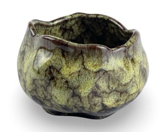May include: A green and brown ceramic planter with a wavy rim. The planter has a mottled glaze with a crackled effect.