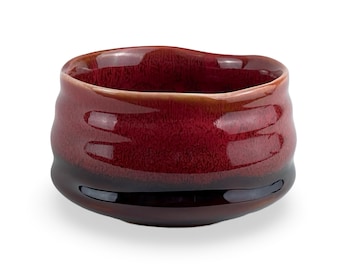 May include: A deep red ceramic tea bowl with a dark brown rim. The bowl has a textured, slightly uneven surface.