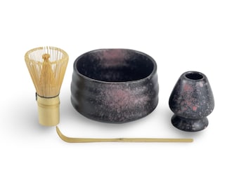 May include: A black and pink speckled matcha bowl, a bamboo whisk, a bamboo matcha scoop, and a bamboo whisk holder.