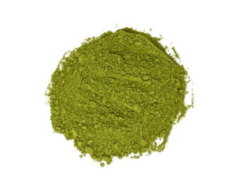 May include: A close-up shot of a pile of finely ground, vibrant green matcha powder against a clean white background. The powder has a slightly textured appearance, suggesting a fresh, high-quality product. The image highlights the natural color and texture of the matcha.