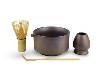 May include: A matcha tea set featuring a brown ceramic bowl with a spout, a bamboo whisk, a whisk holder, and a bamboo scoop. The set is designed for preparing traditional Japanese matcha tea.