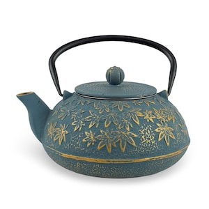 May include: Teapot with a teal finish and gold leaf pattern. The cast iron teapot has a black handle and lid. The teapot is designed for brewing tea and has a spout for pouring.
