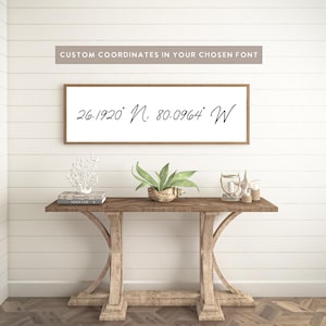 May include: A rectangular wall sign with a light wood frame and a white background featuring the black text 26.1920° N, 80.0964° W in a cursive script. Above the sign, the text CUSTOM COORDINATES IN YOUR CHOSEN FONT is displayed.