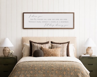 Puede incluir: Escena de dormitorio con una cama con cabecero beige, adornada con cojines decorativos con estampados marrones y beige. Un letrero enmarcado sobre la cama muestra una cita romántica. Dos mesitas de noche verdes con lámparas flanquean la cama.