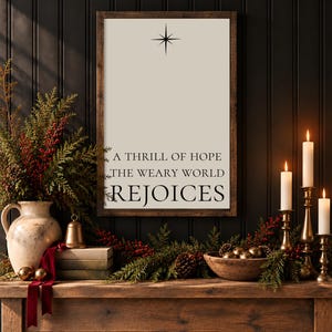May include: A rectangular wooden-framed wall sign with a cream-colored background featuring a black star icon at the top and the black text A THRILL OF HOPE THE WEARY WORLD REJOICES printed in a serif font centered on the surface.