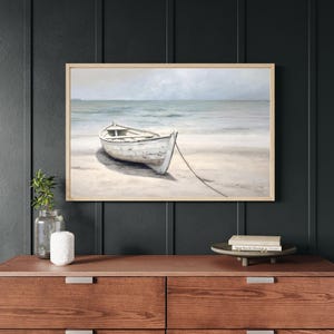 Framed wall art with wood frame featuring a neutral-toned rowboat on a beach with ocean waves in the background, perfect for coastal home decor.