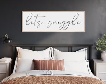 May include: A black metal bed frame with a white headboard and a white duvet cover. The headboard has a wooden frame with a white sign that reads "Let's snuggle".