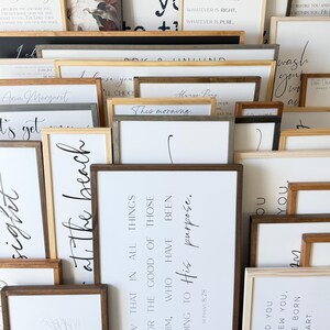 May include: A collection of rectangular wooden framed wall signs featuring white backgrounds with black printed text and illustrations. The signs display various inspirational quotes, scripture verses, and phrases in diverse fonts, arranged in a layered stack.
