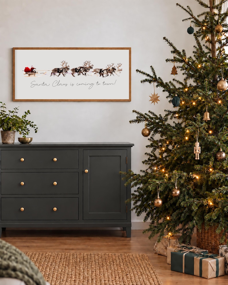 Puede incluir: Un letrero de pared rectangular con marco de madera que presenta un gr&aacute;fico de Santa Claus en un trineo tirado por renos y el texto Santa Claus is coming to town en letras cursivas negras sobre un fondo blanco.