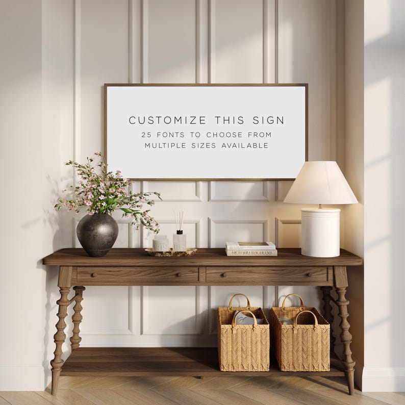 Pu&ograve; includere: Un cartello da parete rettangolare con una sottile cornice marrone che presenta il testo nero CUSTOMIZE THIS SIGN, 25 FONTS TO CHOOSE FROM e MULTIPLE SIZES AVAILABLE. Il cartello &egrave; esposto sopra una console in legno con due cassetti e un ripiano.
