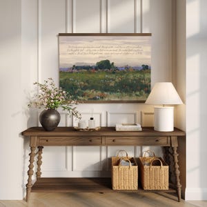 May include: A wooden console table with a landscape painting, a lamp, and decorative items. The painting features a field with text from Ephesians 2:10. Two woven baskets sit below the table.