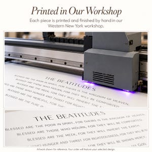 May include: A large industrial printer with a dark grey housing and a glowing purple light is printing black text onto a white surface. The text reads The Beatitudes, followed by several lines of scripture starting with Blessed are the poor in spirit.